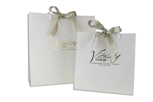 tausendtypentragetaschen - weiße Papiertasche Present mit Baumwollkordeln und cremefarbigem Satinband, Heißfoliendruck gold Motiv Vitality College